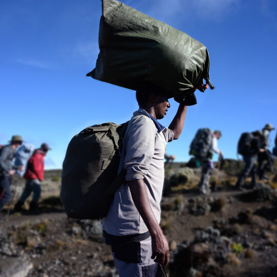 porter with bag on head trekking beside hikers
