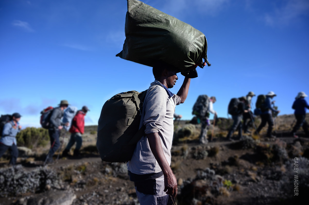 porter with bag on head trekking beside hikers