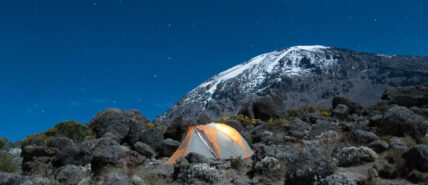 tent under stars at night on kilimanjaro with snowy peak in background