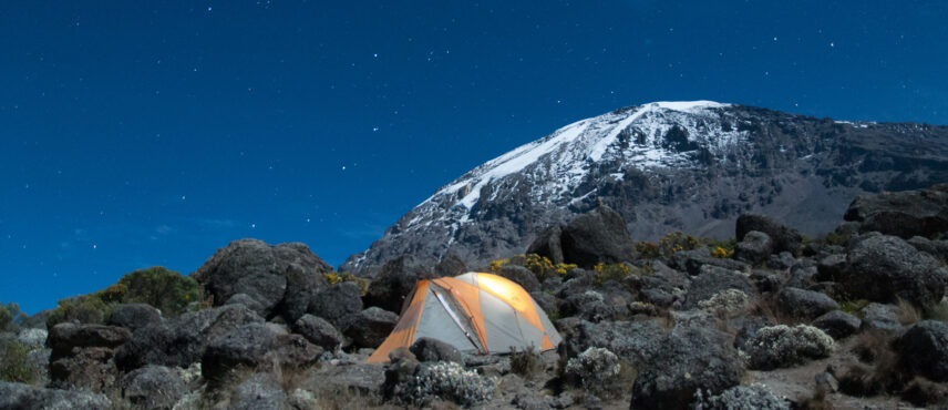 tent under stars at night on kilimanjaro with snowy peak in background