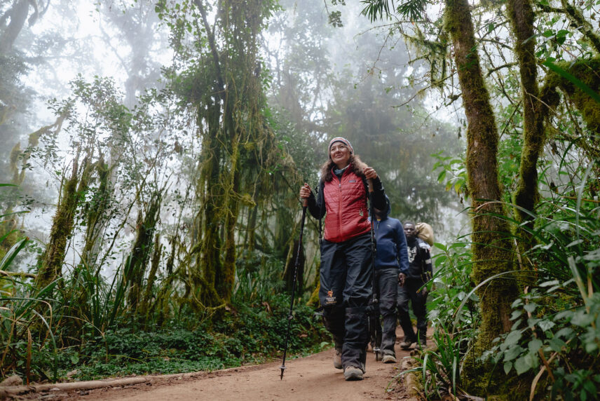 woman trekking through rainforest with porters on kilimanjaro